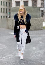 Chiara Ferragni wearing white pants, cropped top, sneaker, black coat with fur collar outside Michae...