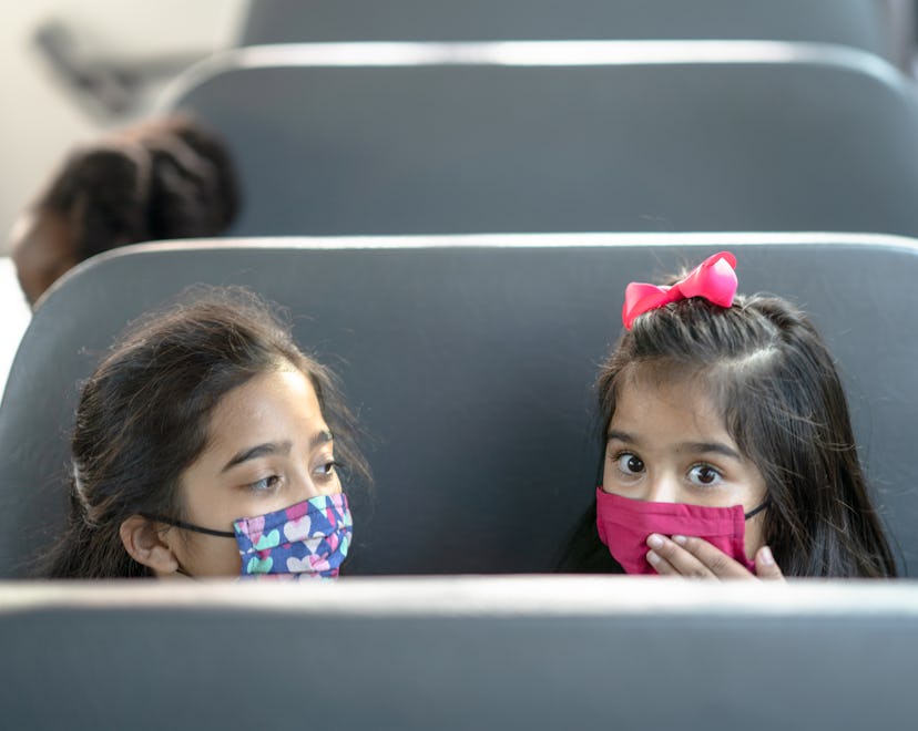 two little girls with face masks on a school bus