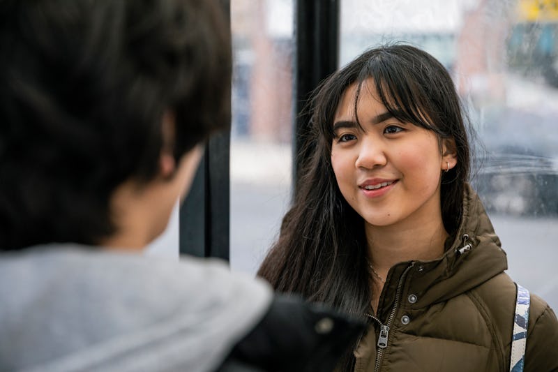 A close-up shot of a young teenage couple standing and talking at a bus shelter, waiting for the bus...