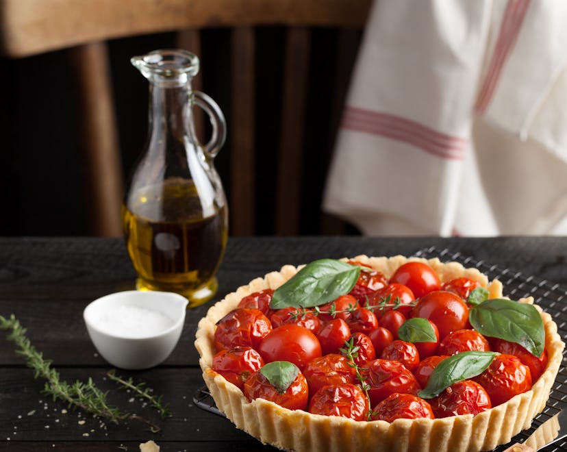 Cherry tomato tart with fresh basil leaves and thyme served on a cooling rack. A black wood plank wa...