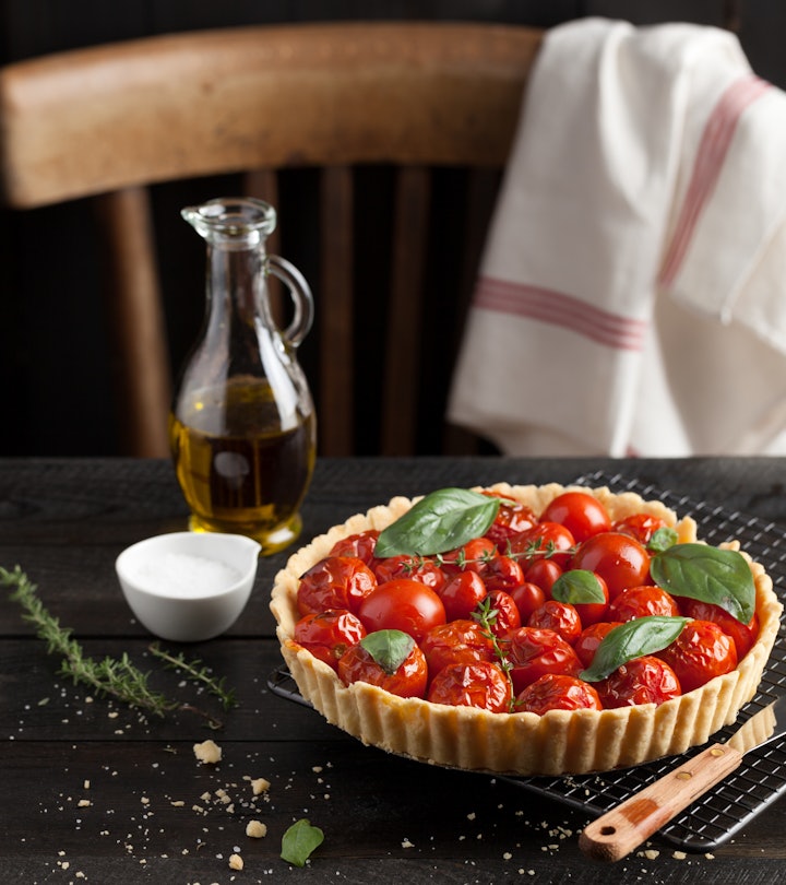 Cherry tomato tart with fresh basil leaves and thyme served on a cooling rack. A black wood plank wa...