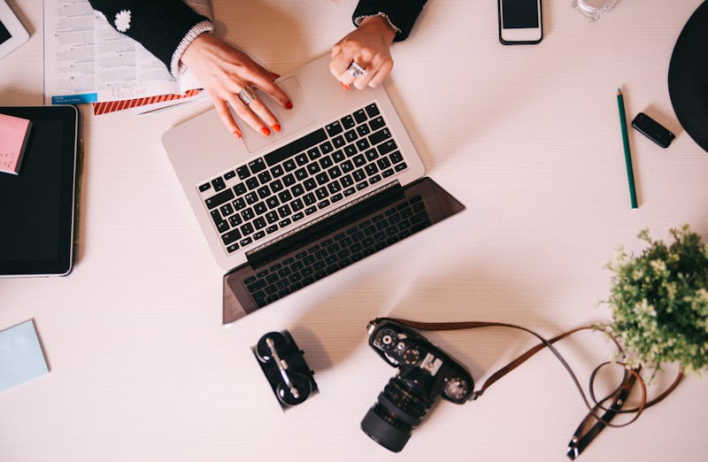 Vintage toned high angle view on a creative work desk. Female hands working on the laptop, some digi...