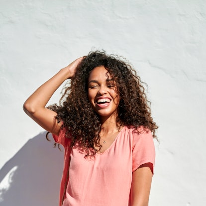 Smiling young woman with curly hair in sunlight, laughing the week of August 2, 2021, which will be ...