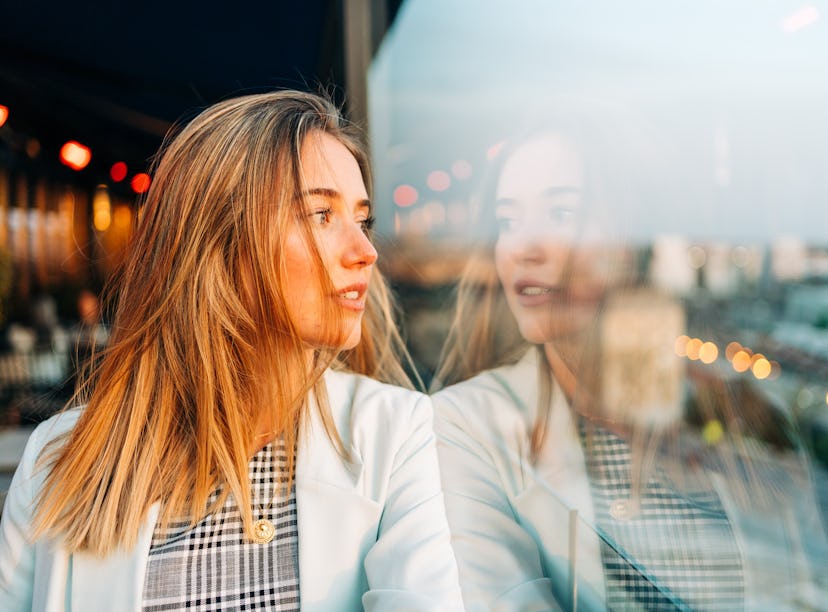 Charming thoughtful female in stylish wear leaning on hand and looking away in roof cafe at sunset