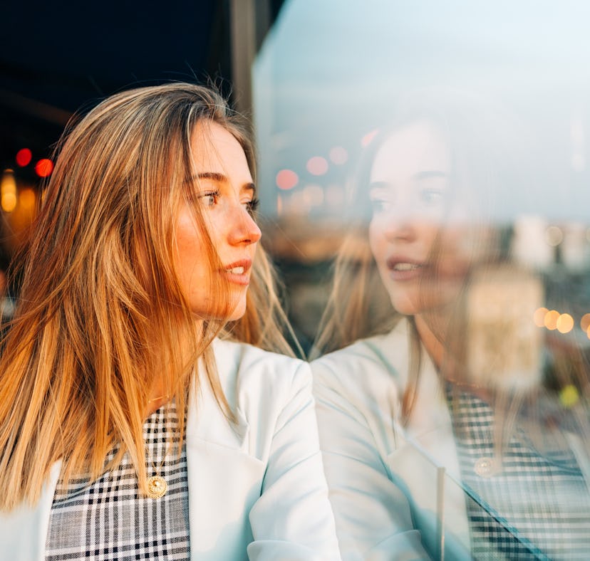 Charming thoughtful female in stylish wear leaning on hand and looking away in roof cafe at sunset