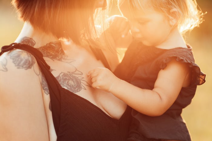 a tattooed mom holding her toddler outside in the sunshine