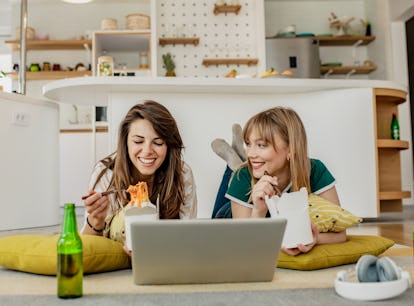 A young couple orders takeout food for a cozy night in, and eats it while watching a show on a lapto...