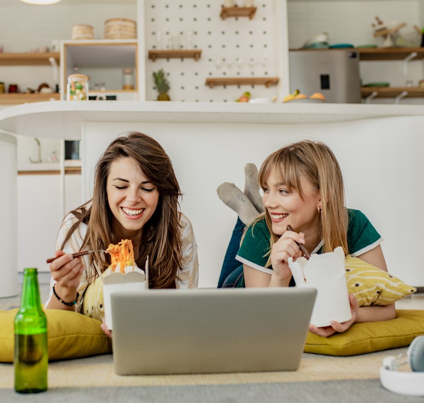 A young couple orders takeout food for a cozy night in, and eats it while watching a show on a lapto...