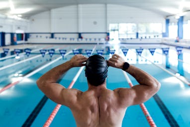 From above back view of anonymous strong male swimmer with naked torso sitting on starting platform ...