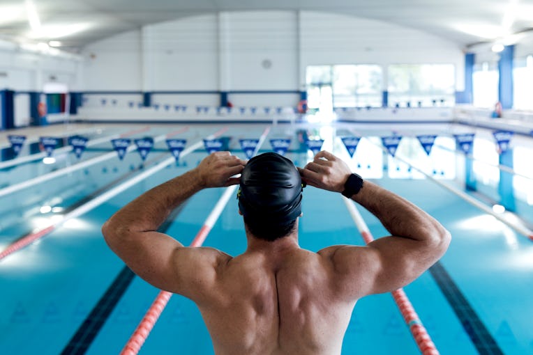 From above back view of anonymous strong male swimmer with naked torso sitting on starting platform ...