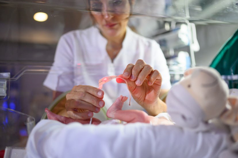 From above woman nurse holding small foot of tiny baby lying in NICU