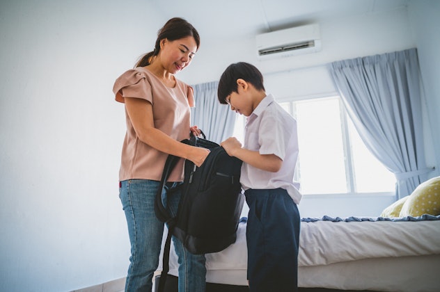 An Asian mum packing backpack and ready lunch box for her son first day of school.