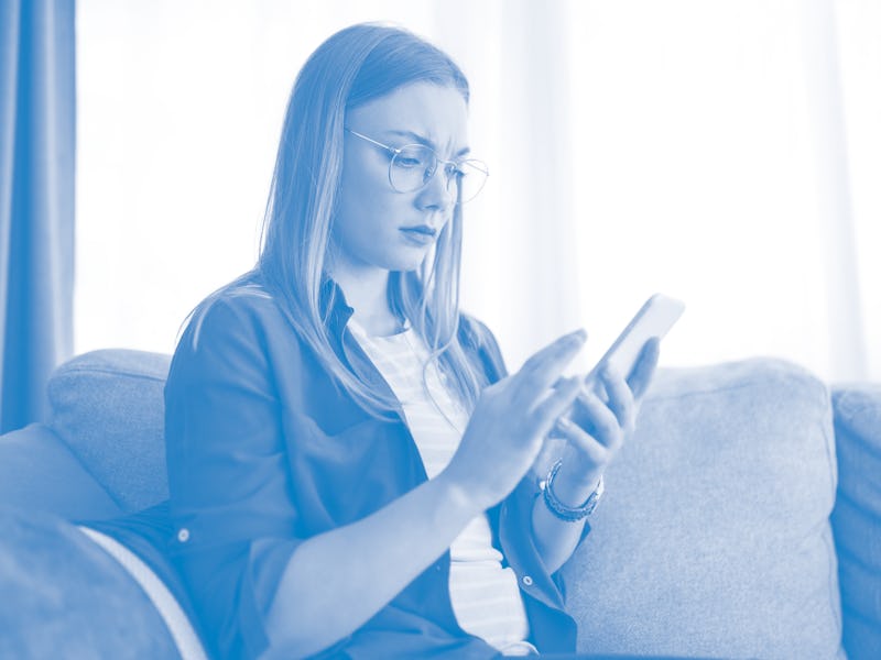 Young worried woman using social media on her phone while resting on sofa i the living room.