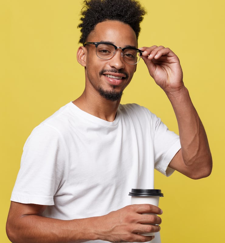 Stylish young afro american man holding cup of take away coffee isolated over yellow background.