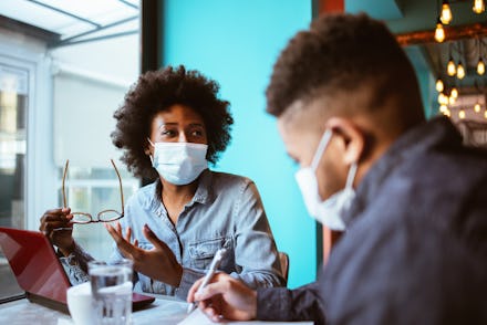 Young African-American business couple with protective face mask talking and working  on a laptop at...