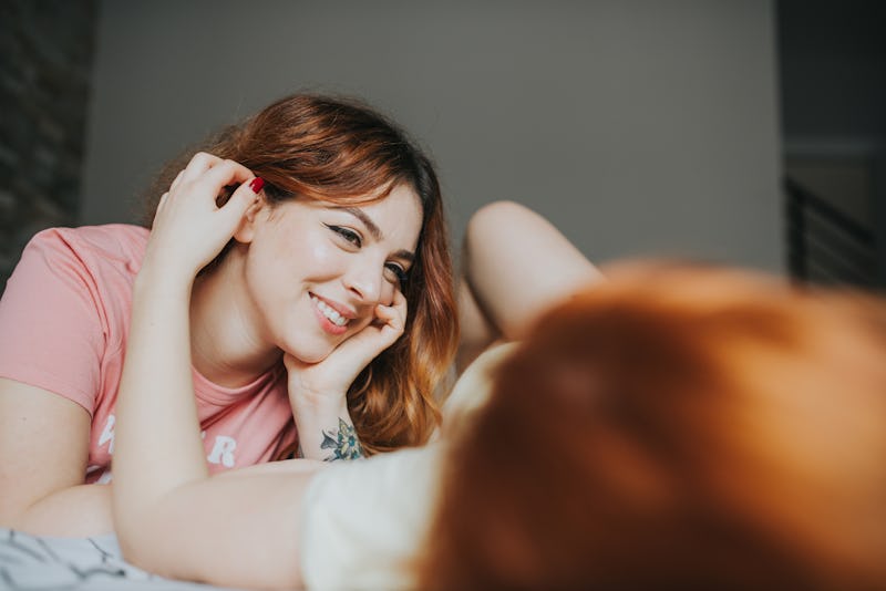 Crop young female girlfriends in pajamas relaxing on bed in bedroom