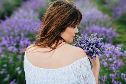 Portrait of a young brunette woman with blue eyes in a white dress on a lavender field and with lave...