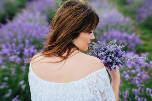 Portrait of a young brunette woman with blue eyes in a white dress on a lavender field and with lave...