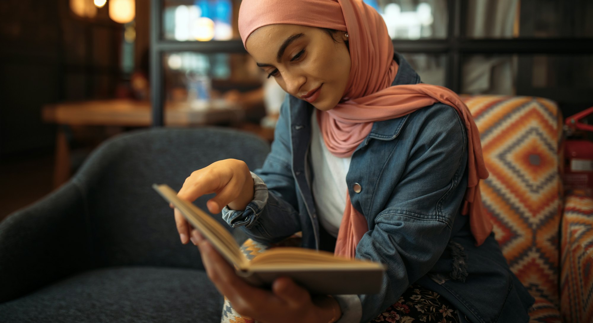 Young muslim woman in hijab reading book at cafe