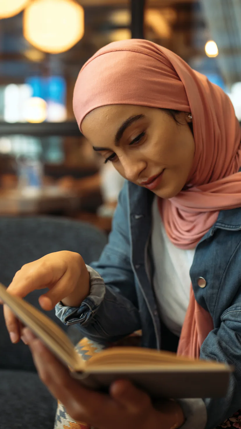Young muslim woman in hijab reading book at cafe
