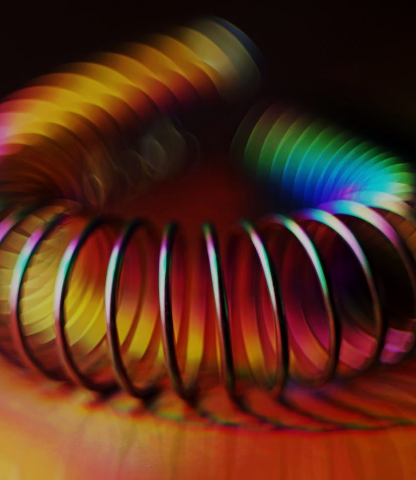 Titanium-coated metal spring on holographic foil with rainbow light effects. Low key lighting.