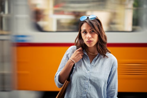 Portrait of beautiful Latino woman on the street, she standing in front of blurred motion tramway on...