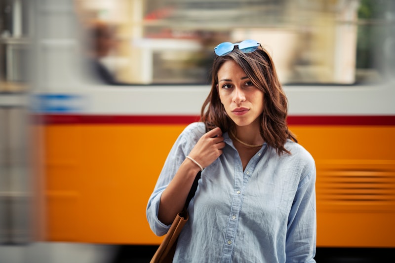 Portrait of beautiful Latino woman on the street, she standing in front of blurred motion tramway on...