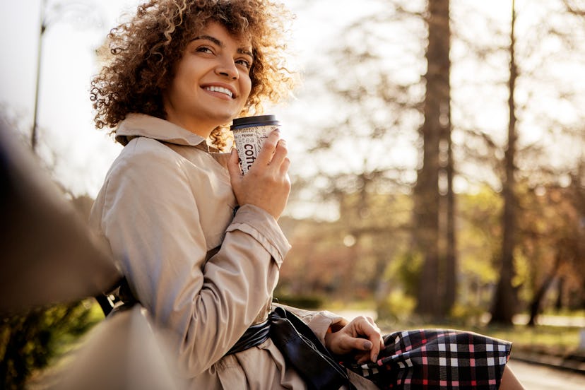 Beautiful young woman smiling with eyes closed drinking a takeaway cup of coffee outside