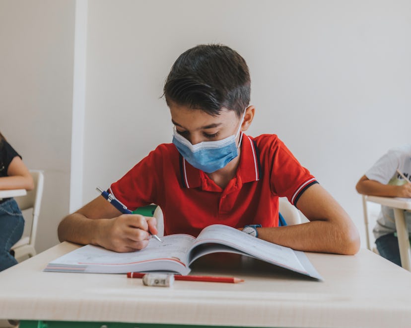 boy with face mask working at school desk