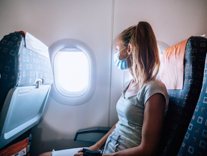Woman sitting inside airplane enjoying flight. 
Tourist wearing facial mask due to Covid-19 crises