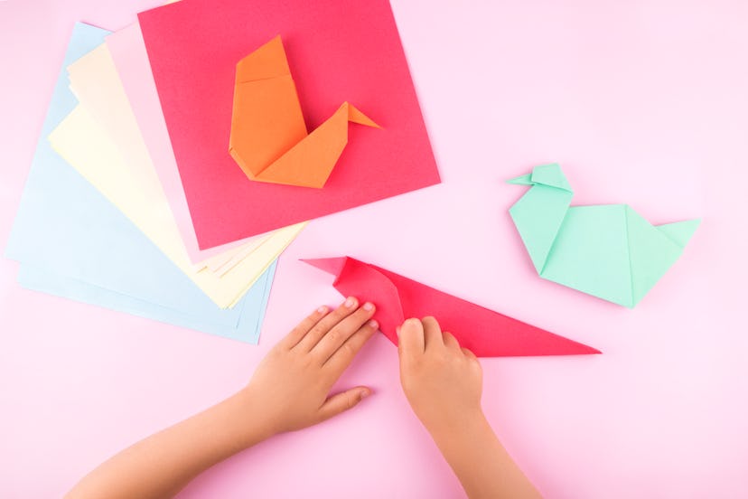 Little girl making origami from colorful paper at the table at home.