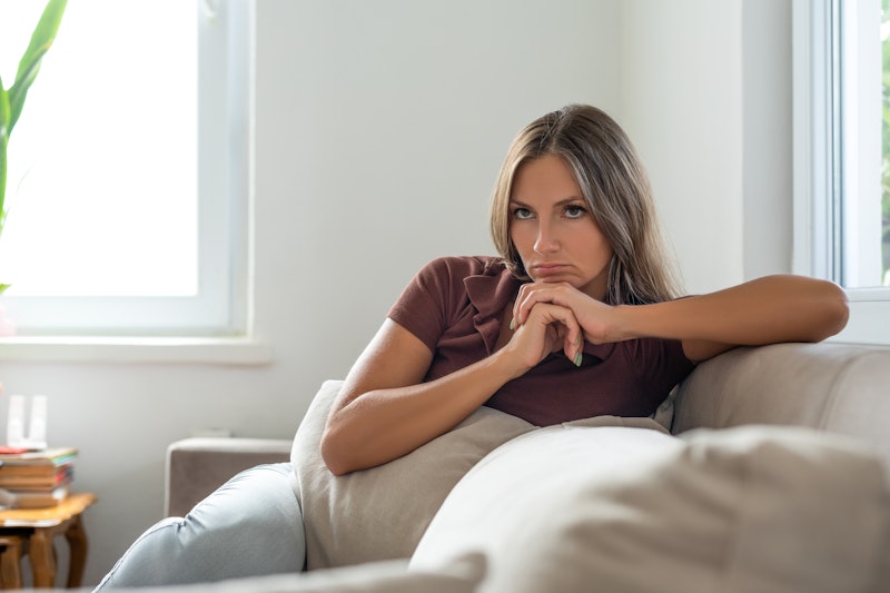 Sad woman sitting on sofa alone at home