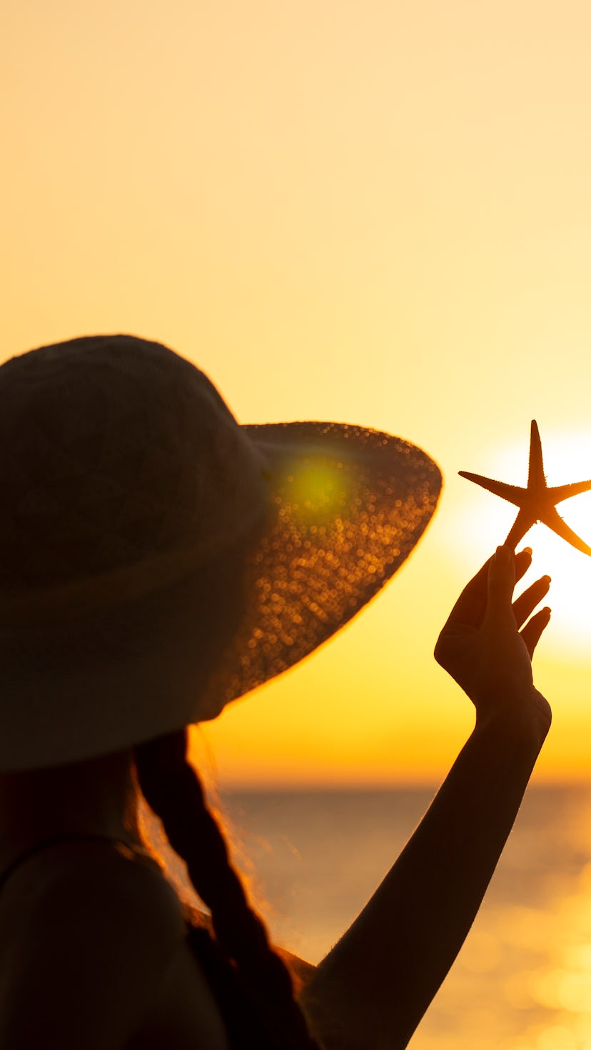young woman in hat with starfish on the beach
