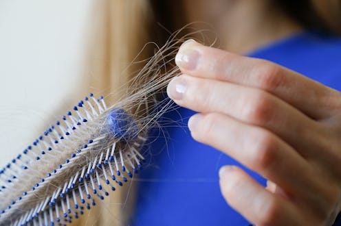 A woman holds a comb in her hands, cleans it from fallen hair after combing, in the bathroom. The co...
