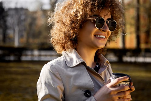 Beautiful young woman smiling wearing sunglasses and drinking a takeaway cup of coffee outside