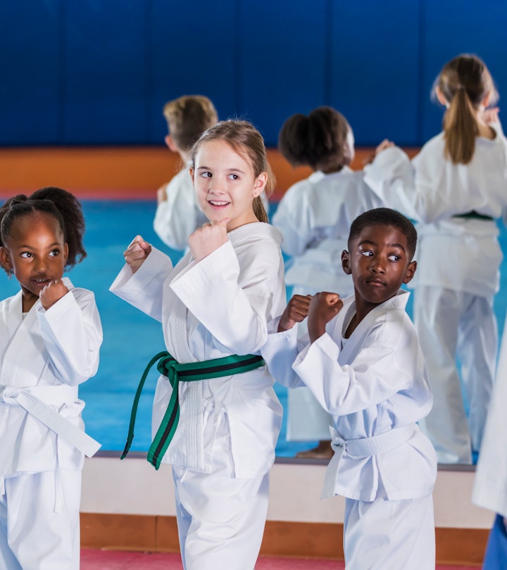 A multi-ethnic group of children, 6 to 9 years old, taking a taekwondo class. They are standing in a...