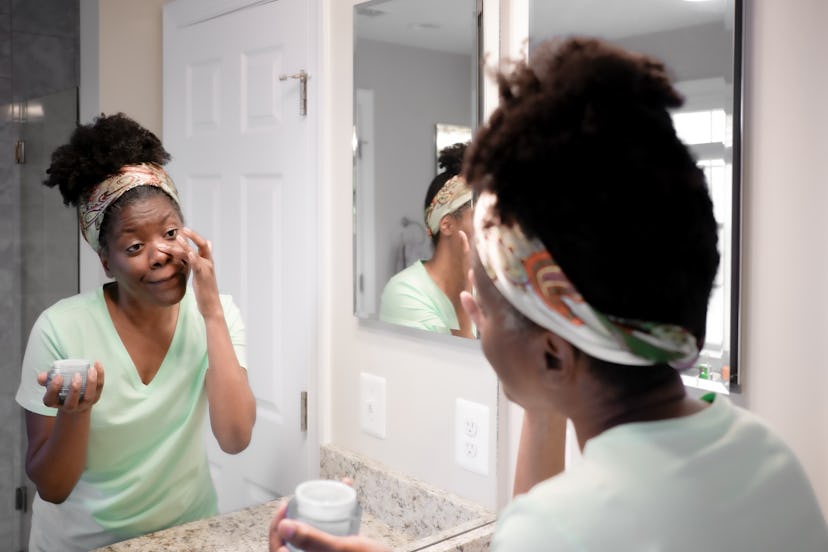 Close-up of mid adult black woman applying facial moisturizer in bathroom mirror