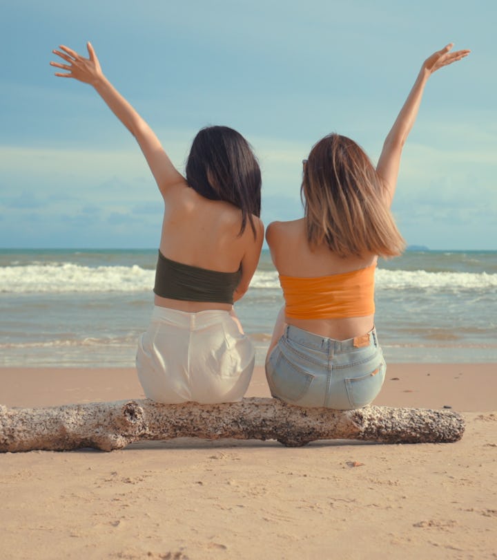 sisters sitting on a piece of driftwood on the beach, looking at the ocean