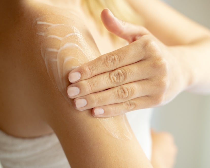 woman putting lotion on arm after shower