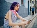 A young woman sits on the side of the street looking at her phone.