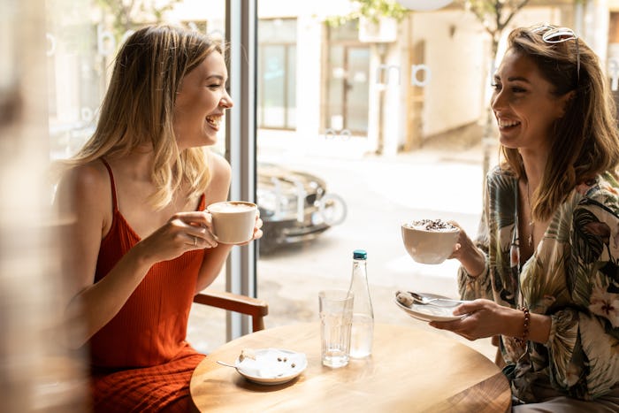 two women friends sitting in cafe drinking coffee