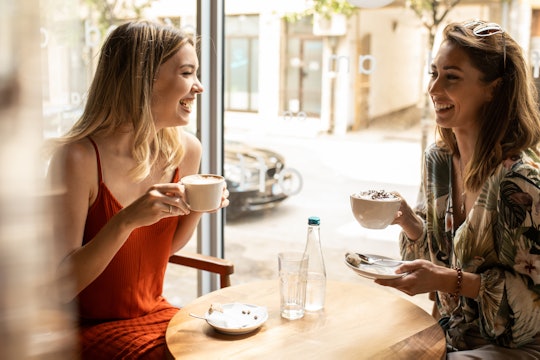 two women friends sitting in cafe drinking coffee