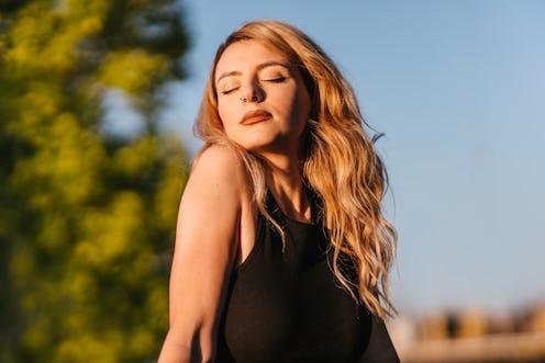 A close-up of a young adult woman with her eyes closed enjoying the Sun in the public park