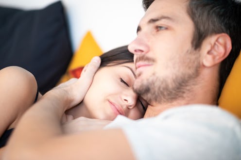 Happy young woman snuggling up to her boyfriend affectionately with eyes closed in bed in the mornin...
