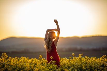 Linda jovem vestindo vestido vermelho brilhante no campo amarelo de planta de canola. O campo é espaçoso...