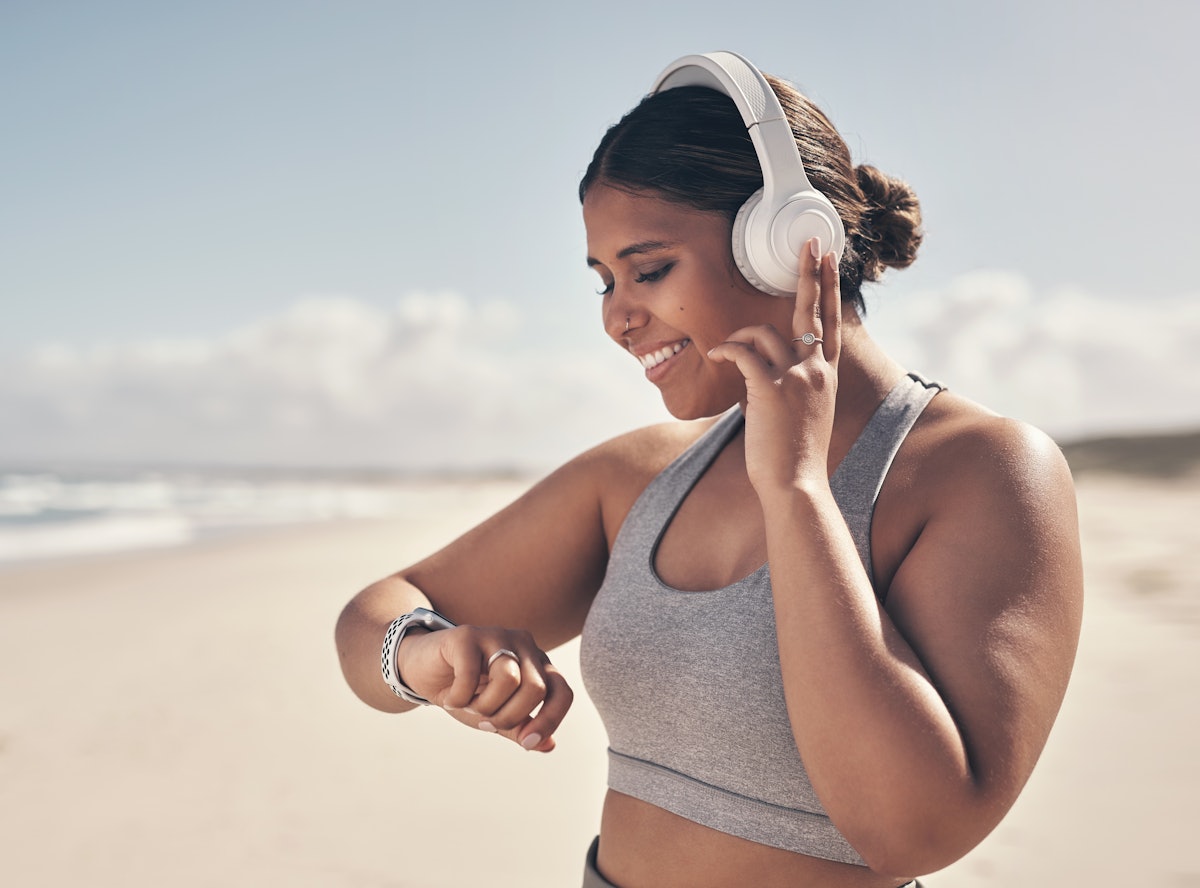 A person wears headphones while checking their watch during a beach run. Running on a beach works yo...
