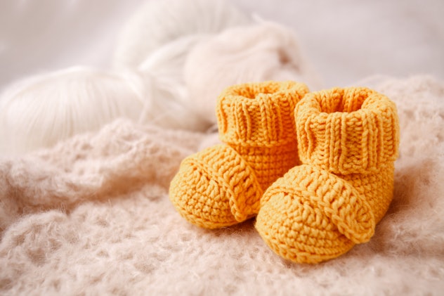 Image of marigold-colored crochet baby booties, resting on a cream-colored crochet blanket. 