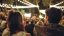 Back view of young couple sitting and enjoying in a open night music festival outdoors on summer