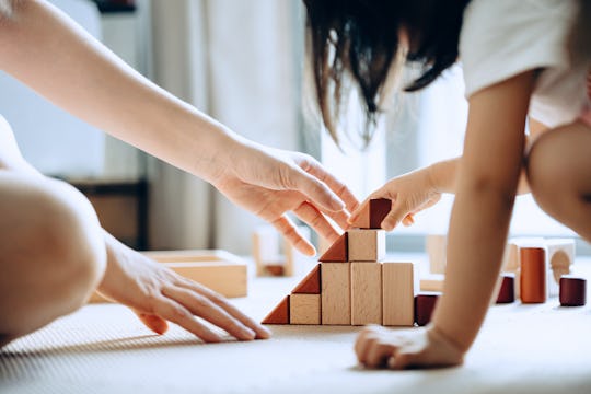 Close up of mother and little daughter sitting on the floor playing with wooden building blocks toge...