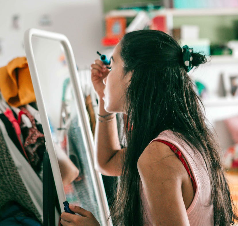 a young woman sitting in front of her bedroom mirror, learning how to apply makeup